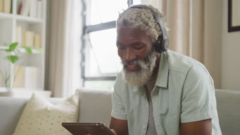 video of african american senior man using tablet and headphones