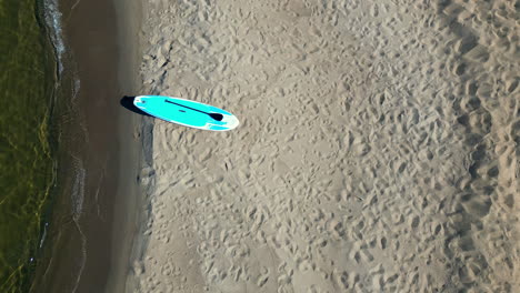 paddling board left on sandy beach, aerial top down view