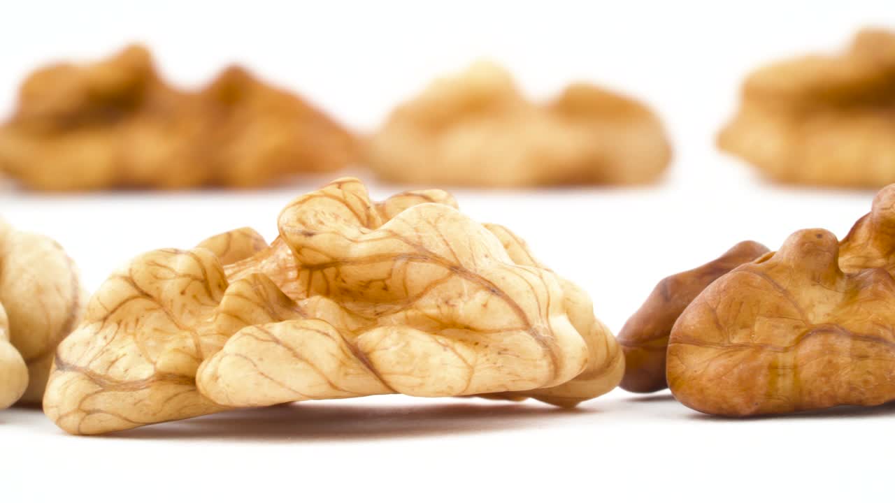 Two rows of walnuts without the shell are moving horizontally from one side of the frame to other. Isolated on the white background. Close-up. Macro.