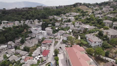 Aerial-over-Gjirokastër-city-with-Gjirokastra-Fortress-on-hillside,-Albania