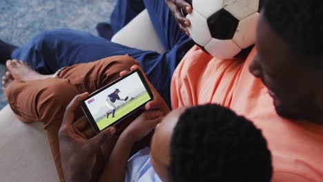 composite of father and son at home watching baseball game on smartphone