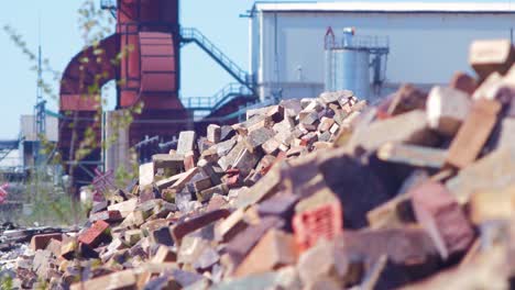 Exterior-view-of-abandoned-Soviet-heavy-metallurgy-melting-factory-Liepajas-Metalurgs-territory,-piles-of-debris-and-old-bricks,-sunny-day,-rusty-base-of-a-chimney,-medium-shot