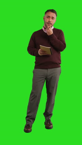 man standing in front of a green screen, holding a notebook and pen