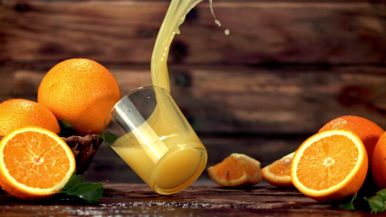 Appelsinjuice sprøjter og spilder fra et glas med friske appelsiner