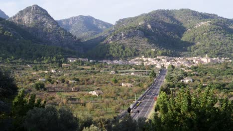 Inmitten-Eines-Ruhigen-Mallorquinischen-Herbstabends-überquert-Ein-Einzelnes-Auto-Die-Malerische-Straße-Nach-Caimari,-Eingebettet-Zwischen-üppigen-Hügeln,-Die-Die-Friedliche-Essenz-Des-Dorfes-Einfangen