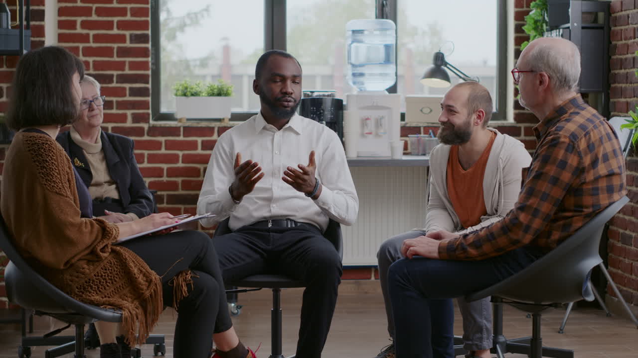 African american man making confession about addiction and rehabilitation with people at group therapy