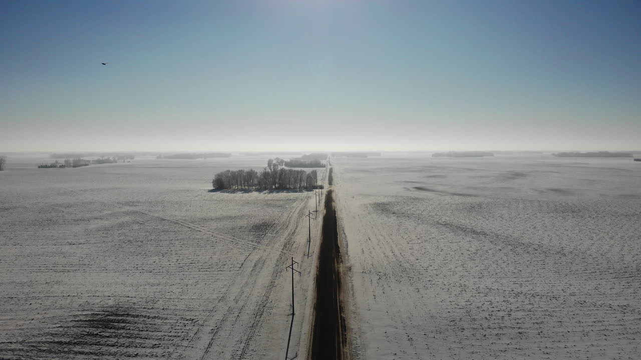 Rising aerial drone shot of empty dirt road in winter with snow