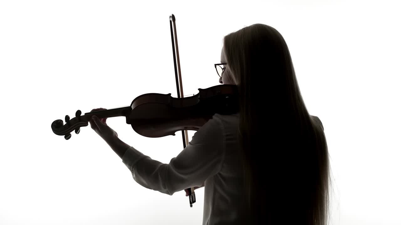 Woman with glasses plays the violin with bow, a black silhouette on white background. Violinist woman plays a musical instrument violin in the studio