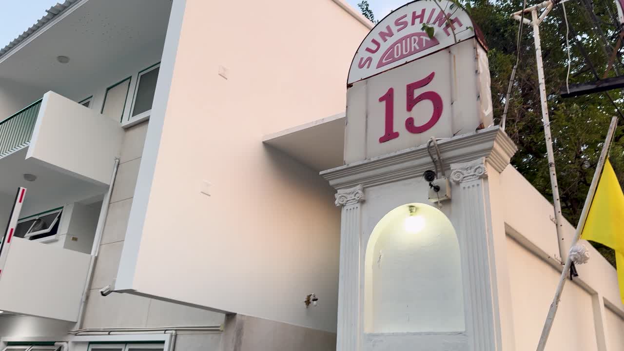 Una cámara de mano recorre la puerta de entrada y la fachada blanca de un apartamento de Bangkok.