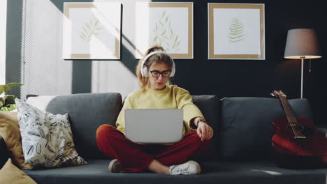 woman in headphones singing and using laptop on sofa at home