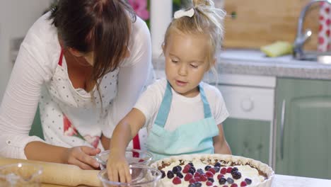 young mother watching her little daughter baking