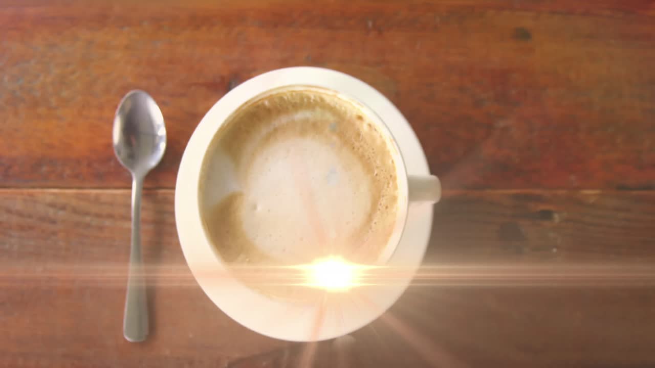 Animation of lens flare moving over overhead view of coffee cup with spoon on wooden table