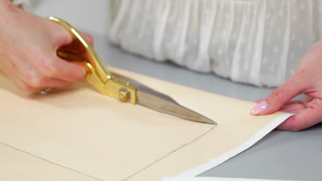 young female designer with tape-line on her neck standing in dressmaking studio and drawing lines with chalk and rule. female couturier in atelier cutting out a pattern for future clothes.