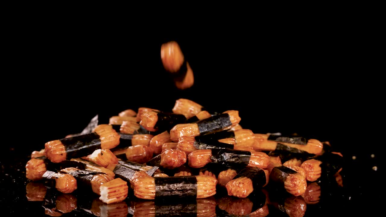 Crunchy Japanese rice crackers drop onto glossy black background, illuminated by dramatic studio lighting