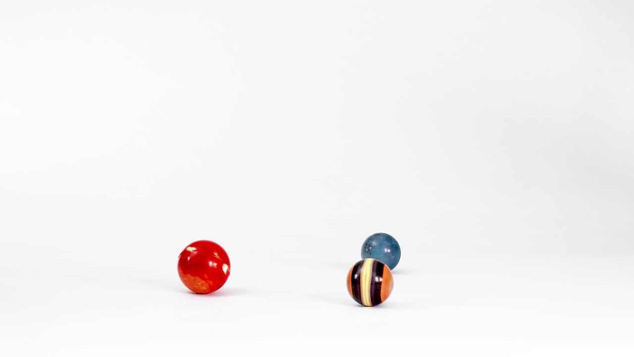 Kelereng planet Bumi dan bola mainan warna-warni bergulir di atas permukaan latar belakang studio putih bersih.