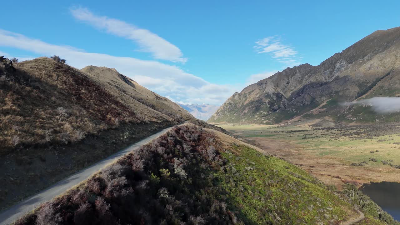 Aerial footage captures winding mountain roads and stunning landscapes in Queenstown, New Zealand, under clear blue skies