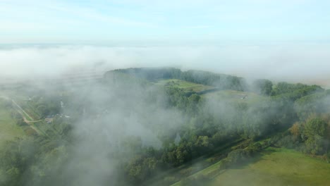 Under-the-layer-of-mist-opens-up-a-view-of-the-treetops-in-Suffolk,-United-Kingdom
