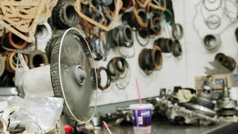 a cluttered workshop with auto parts and a fan