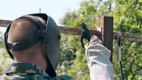 slow-motion-backside-view-man-unwelds-metal-plank-from-fence