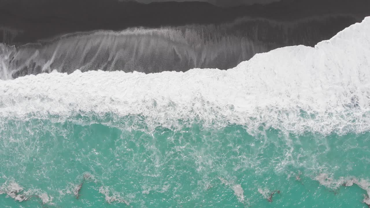 Epic aerial view from great height down on bright white waves of turquoise ocean washing the dar black sand beach of New Zelaand coast in 4k during clear sunny day.