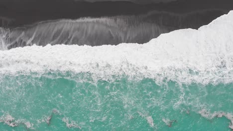 epic aerial view from great height down on bright white waves of turquoise ocean washing the dar black sand beach of new zelaand coast in 4k during clear sunny day.