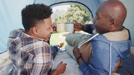 Feliz-Padre-Afroamericano-E-Hijo-Adulto-Haciendo-Un-Brindis-Con-Tazas-De-Café-En-Tienda,-Cámara-Lenta