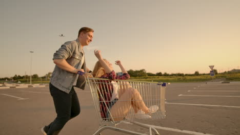 cheerful people a couple a man and a woman at sunset ride on supermarket trolleys in slow motion.