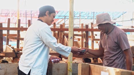 muslim man paying money or making a deal for buying goat at the cattle farm. islamic and eid al adha concept.