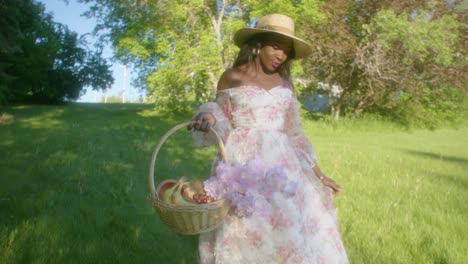 black woman walking in the park smiling in dress with basket low angle