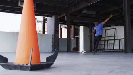 Hombre-Afroamericano-Pateando-Una-Pelota-De-Fútbol-En-Un-Edificio-Urbano-Vacío