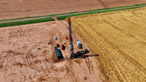 industrial machine with set up rig for oil drilling. drone footage around the derrick boring natural resources in the field near wheat plantation.
