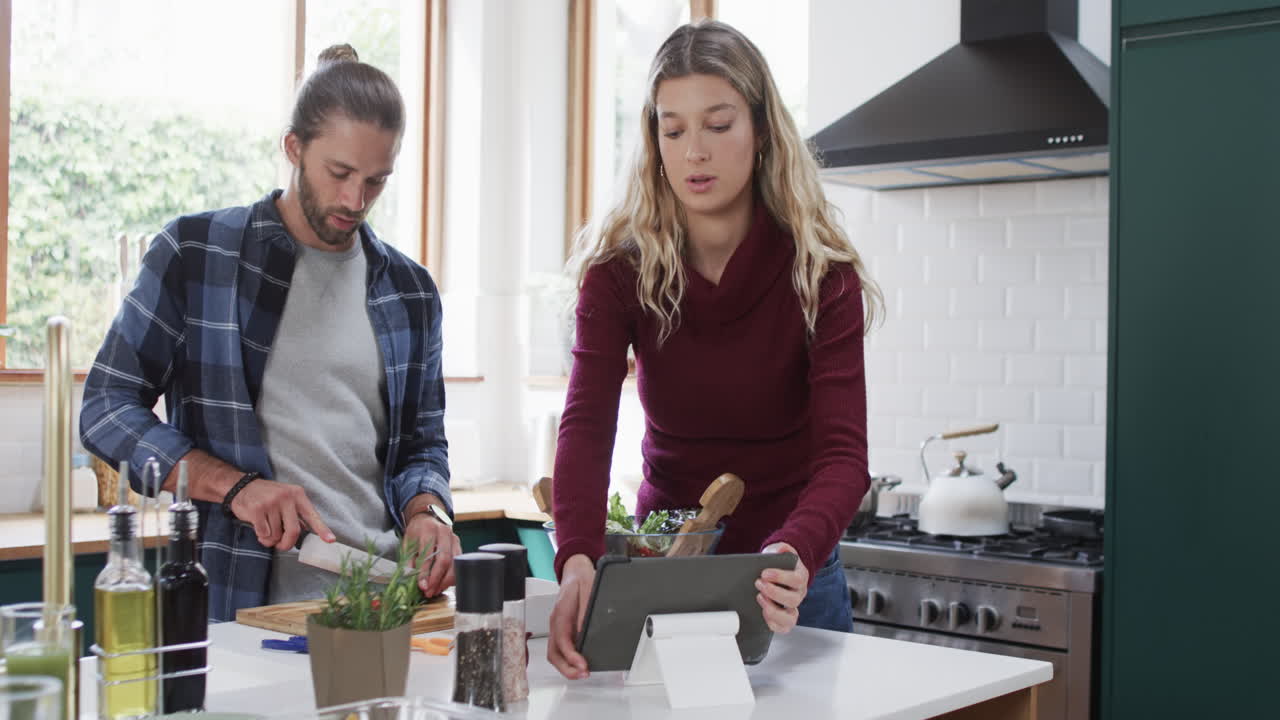 pareja diversa preparando la cena en la cocina usando la tableta en casa, en cámara lenta