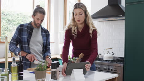 diverse couple preparing dinner in kitchen using tablet at home, in slow motion