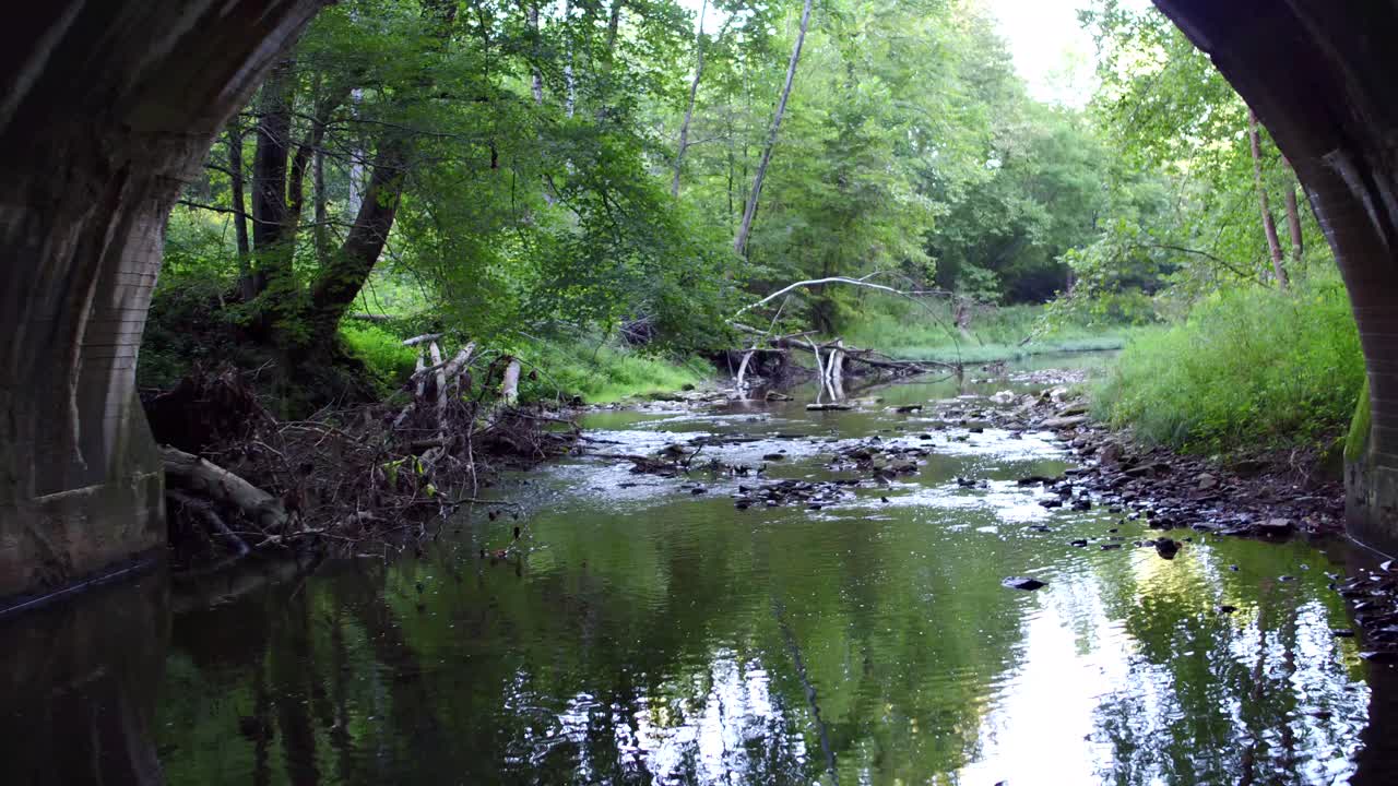 숲속의 오래된 돌다리와 강 아래에서 느린 드론 촬영