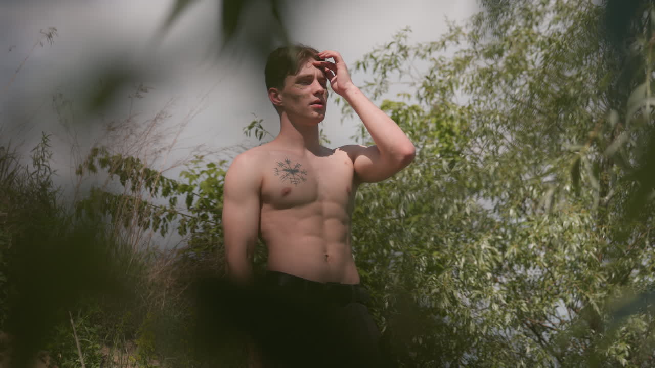 fighter exhaling in relief gazing river ahead framed by leafy branch blur, headband loosened, sunlit muscles relaxing after strenuous climb across steep bank and dense vegetation conveying triumph