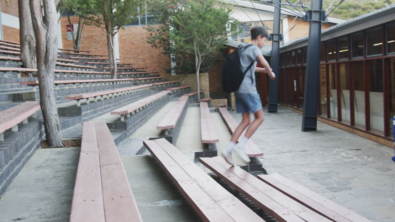 Running through school courtyard, boy with backpack jumping over benches, copy space