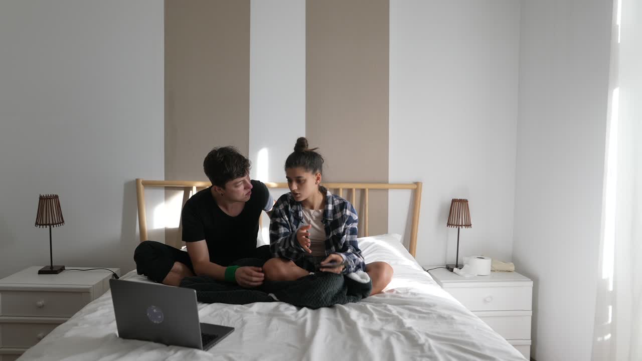 Couple Relaxing Together on a Bed with a Laptop and Smartphones