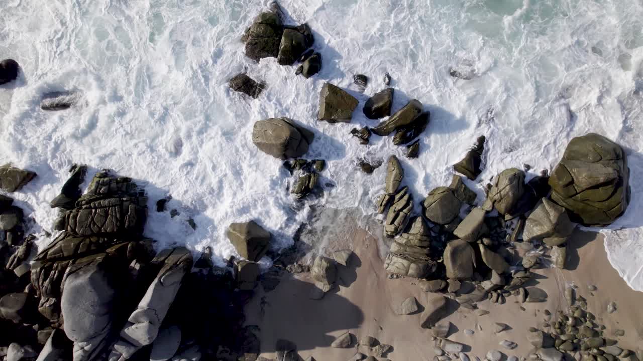 Drone flyver tæt på klipper på stranden, mens bølger slår ind over dem