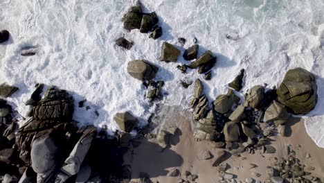 Drone-Empujando-Rocas-En-La-Playa-Mientras-Las-Olas-Rompen-Sobre-Ellas