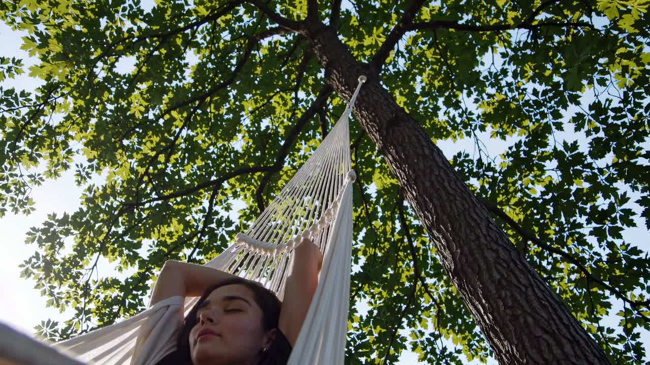Low-angle video of a person relaxing in a hammock under a tree, capturing a serene, peaceful vibe