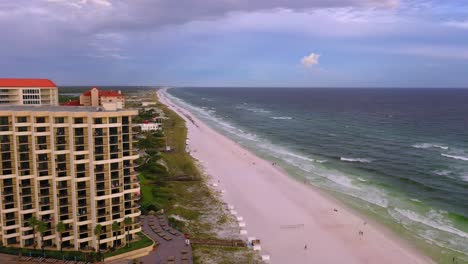 vista de drones volando por la playa de arena blanca de san destin fl más allá de algunos condominios durante la hora dorada con algunas nubes oscuras en el cielo