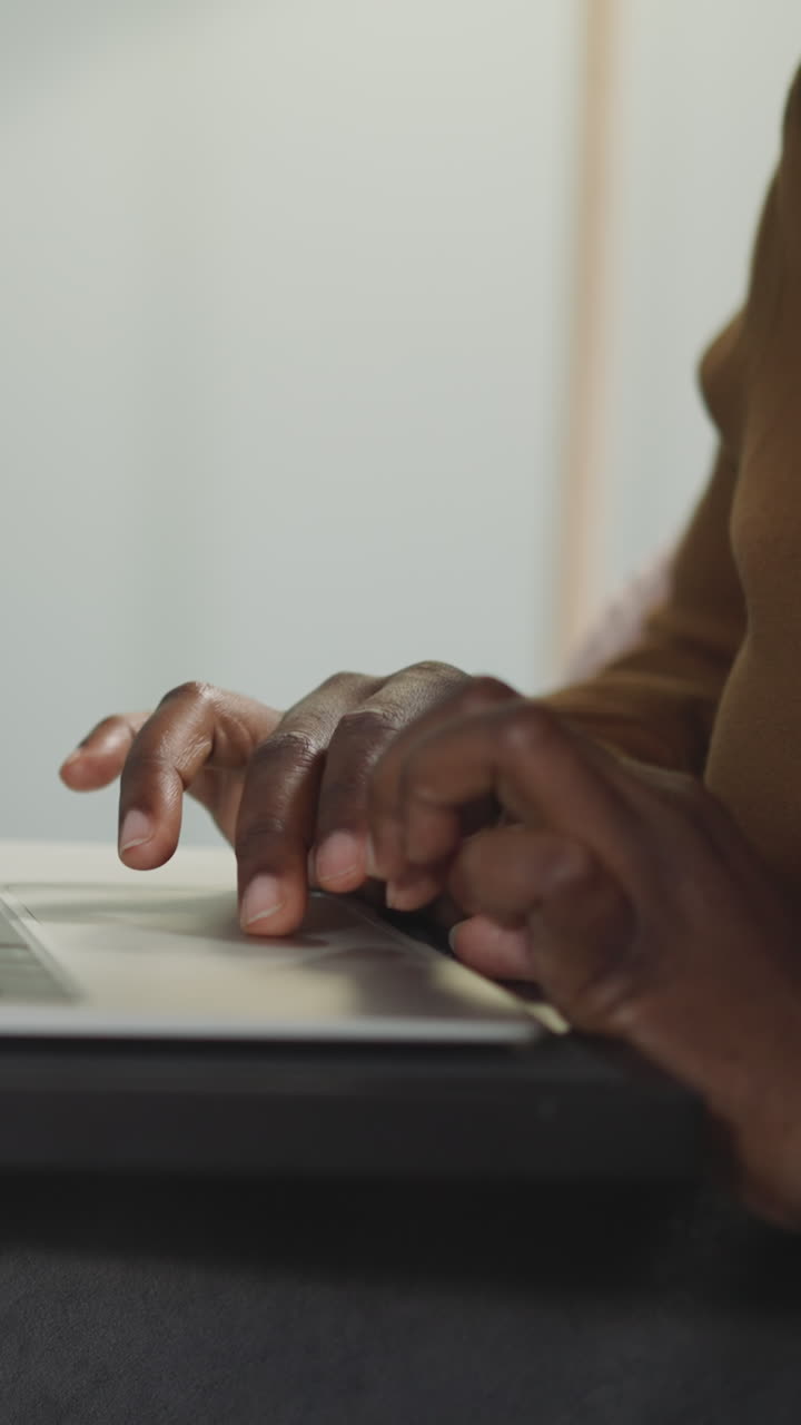 African American woman works on laptop sitting at table on blurred background. Hands of female freelancer checks websites on computer closeup