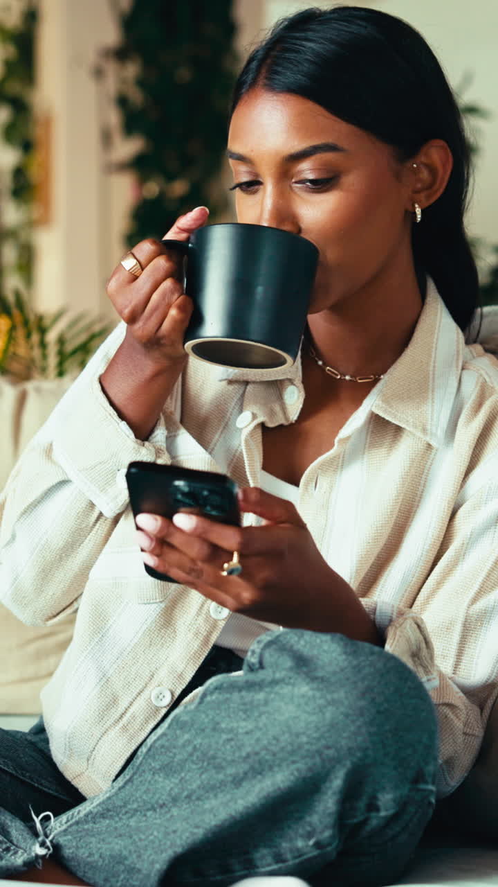 Ung kvinde drikker kaffe og bruger smartphone derhjemme