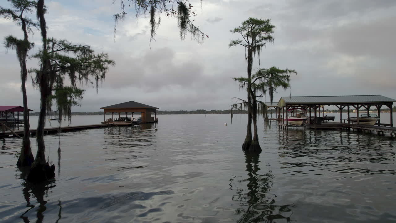 disparo de dron pasando por cipreses y musgo español en dirección al lago con muelles