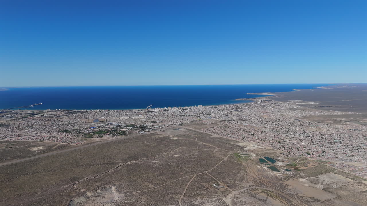 Aerial establishing panoramic overview of Puerto Madryn cityscape, showing its coastline and urban layout under bright sunlight
