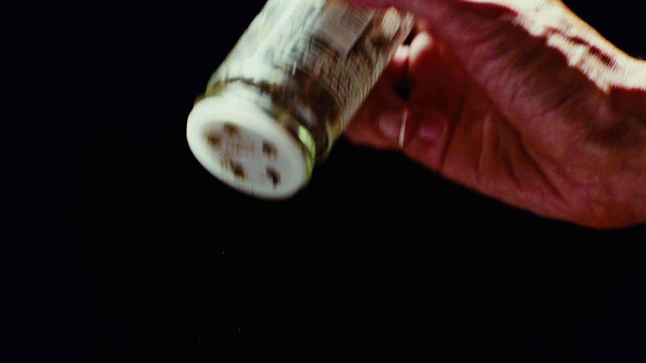 Chef's hand elegantly sprinkling Italian herbs and seasonings against black background. Slow motion shot with professional studio lighting