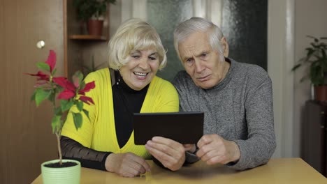 Pretty-mature-senior-couple-grandparents-enjoy-online-shopping-on-tablet-at-home