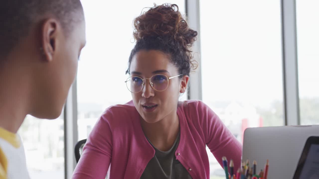 Duas empresárias criativas e diversas felizes usando laptops e conversando à mesa em um ambiente moderno