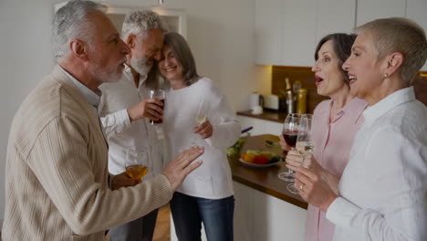 group of cheerful senior friends laughing and drinking wine in the kitchen