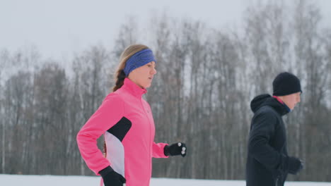 positive beautiful young healthy couple running with sportswear through the forest in the winter morning